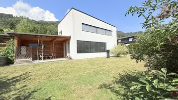 Modernes Haus mit weißer Fassade, großem Garten und überdachter Terrasse im Grünen.