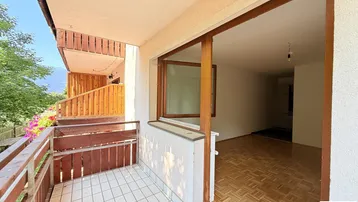 Geräumiger Balkon mit Fliesenboden und Holzelementen, bietet Zugang zu einem hellen Innenraum.