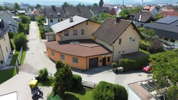 Luftaufnahme eines Wohnhauses mit Anbau und umliegender Nachbarschaft in sonniger Lage.