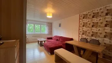 Gemütlicher Wohn-Essbereich mit rotem Sofa, Holztisch und Blick ins Grüne durch das Fenster.