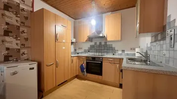 Funktionale Küche mit hellen Holzschränken, grauer Arbeitsplatte und gefliestem Spritzschutz.