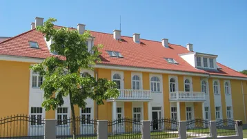 Gelbe Fassade eines Mehrfamilienhauses mit rotem Ziegeldach und weißen Balkonen.