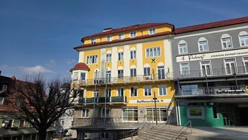 Traditionelles Mehrfamilienhaus mit gelber Fassade, Balkonen und rotem Mansarddach in städtischer Umgebung.