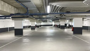 Geräumige Tiefgarage mit vielen markierten Stellplätzen, Betonwänden und sichtbaren Installationen an der Decke.