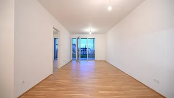 Heller, leerer Raum mit Parkettboden und Zugang zu einem Außenbereich durch große Glastüren.