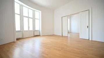 Helles Wohnzimmer mit großen Fenstern, Parkettboden und hohen Decken, bereit zur individuellen Gestaltung.