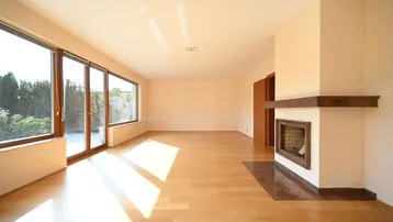 Helles Wohnzimmer mit großen Fenstern, Holzboden und einem integrierten Kamin, der viel Tageslicht hereinlässt.