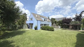 Großzügiger Gartenbereich mit gepflegtem Rasen und einem blauen Einfamilienhaus im Hintergrund unter blauem Himmel.