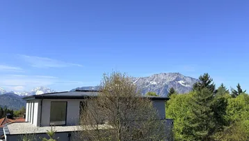 Modernes Gebäude in grüner Umgebung mit Bergblick unter klarem blauem Himmel.