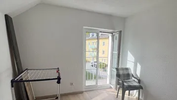 Heller Raum mit Laminatboden und französischem Balkon, der Tageslicht hereinlässt.