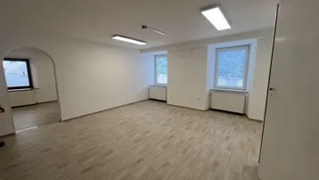 Helles, leeres Zimmer mit Laminatboden, weißen Wänden und zwei Fenstern, ideal für Wohn- oder Bürozwecke.