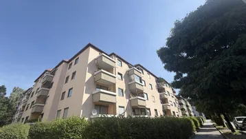 Mehrfamilienhaus mit mehreren Balkonen und gepflegter Hecke unter blauem Himmel.