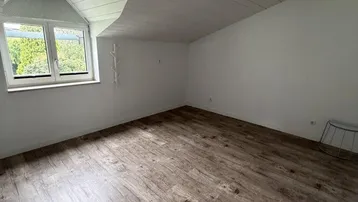 Heller Raum im Dachgeschoss mit Laminatboden, Dachschräge und Fenster mit Grünblick.