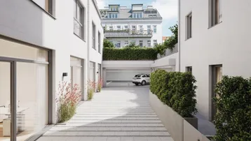 Zufahrt zur Tiefgarage zwischen modernen Gebäuden mit weißer Fassade und begrünten Bereichen.