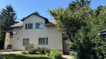 Helles Einfamilienhaus mit Satteldach und gepflegtem Vorgarten unter blauem Himmel.