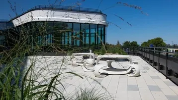 Moderne Dachterrasse mit stilvollen Sitzgelegenheiten und Blick auf das geschwungene Gebäude.