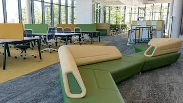 Moderner Großraumbüro-Bereich mit flexiblen Arbeitsplätzen und bequemen Sitzgelegenheiten in Grün- und Beigetönen.