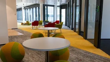 Moderner Bürobereich mit farbenfrohen Sitzgelegenheiten und Tischen, ideal für Pausen und informelle Treffen.