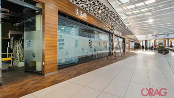 Heller, moderner Ladenkorridor in einem Einkaufszentrum mit Holzverkleidungen, Glasfronten und weißen Bodenfliesen.