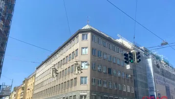Gebäude an einer Straßenecke mit vielen Fenstern und Gerüsten an angrenzenden Gebäuden unter blauem Himmel.