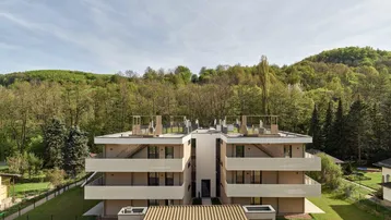 Modernes Mehrfamilienhaus mit mehreren Balkonen und Terrassen, eingebettet in eine grüne Hügellandschaft.