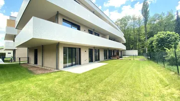 Moderne Wohnanlage mit großzügiger Rasenfläche und Terrasse im Erdgeschoss.