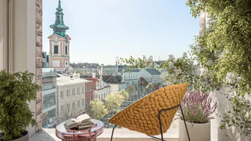 Heller Balkon mit bequemer Sitzgelegenheit und weitem Blick über die Stadt mit Kirchturm.
