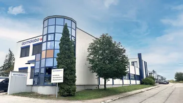Modernes Geschäftsgebäude mit Glasfassade und blauen Akzenten unter blauem Himmel.