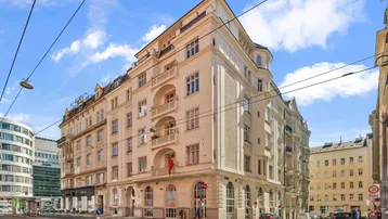 Historisches Eckgebäude mit klassischer Architektur und Balkonen an einer belebten Stadtstraße unter blauem Himmel.