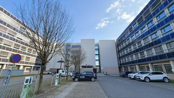 Moderne Bürogebäude mit Photovoltaikanlagen an den Fassaden und Ladestationen für Elektrofahrzeuge auf dem Parkplatz.