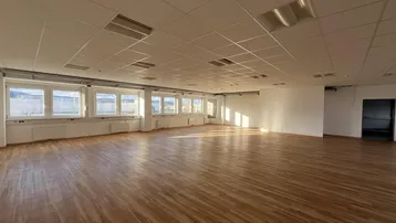 Großer, heller Büroraum mit Holzfußboden und vielen Fenstern, ideal für flexible Arbeitsplatzgestaltung.