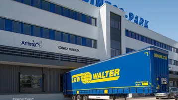Blauer LKW an einer Laderampe eines modernen Bürogebäudes im Business Park.