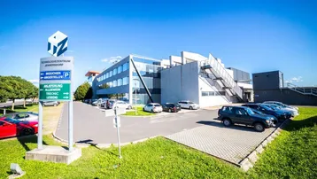 Modernes Technologiezentrum mit Glasfassade und großem Parkplatz unter blauem Himmel.