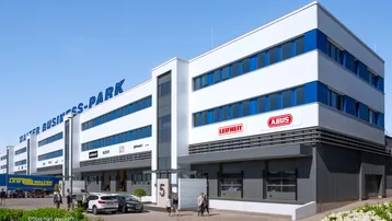Modernes Geschäftsgebäude mit blauen Akzenten und Parkplätzen vor dem Eingangsbereich des Business-Parks.