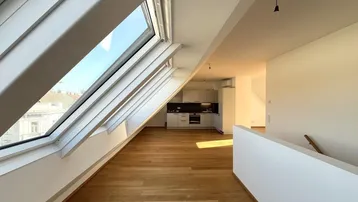 Helles Dachgeschoss-Apartment mit offener Wohnküche, Holzboden und großen Dachfenstern, die viel Licht hereinlassen.