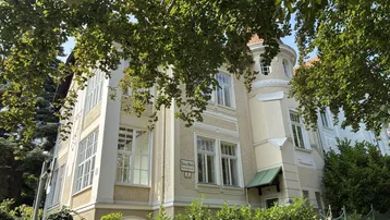 Historische Villa mit markanter Architektur und üppigem Grün umgeben.
