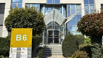 Eingangsbereich eines modernen Bürogebäudes mit Glasvordach und Beschilderung für die Einheit B6.