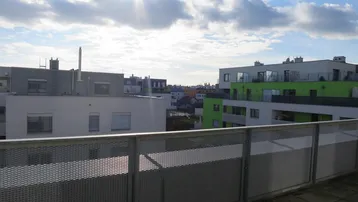 Terrasse mit Metallgeländer und Blick auf moderne Wohngebäude unter bewölktem Himmel.