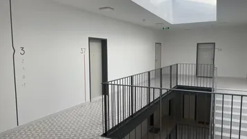 Heller Treppenhausbereich mit Oberlicht, modernen Geländern und gemustertem Bodenbelag in einem Neubau.
