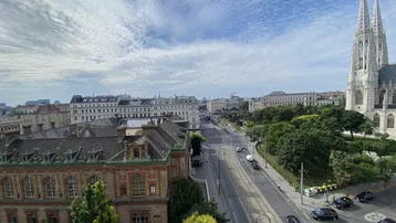 Panoramablick über eine belebte Stadtstraße mit historischen Gebäuden, Bäumen und einer imposanten Kirche.