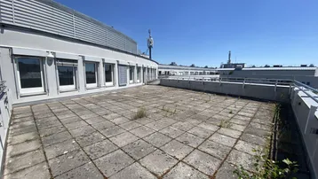 Weitläufige Dachterrasse mit Betonplatten und Blick auf die Umgebung unter blauem Himmel.