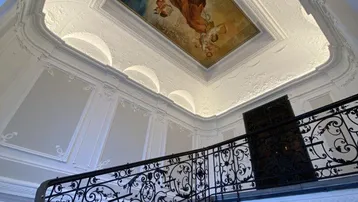 Prunkvolles Treppenhaus mit kunstvollem Deckengemälde, Stuckverzierungen und schmiedeeisernem Geländer.