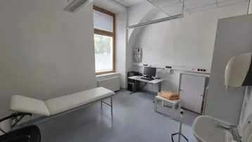 Funktionaler Behandlungsraum mit Untersuchungsliege, Waschbecken und Fenster.