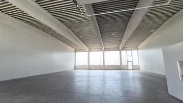 Großer, leerer Gewerberaum mit hohen Decken, Betonboden und viel Tageslicht durch große Fenster.