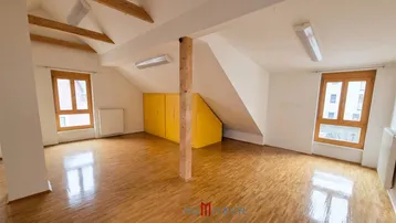 Geräumiger Dachbodenraum mit Holzbalken, schrägen Wänden und Parkettboden, ideal für Wohn- oder Arbeitszwecke.
