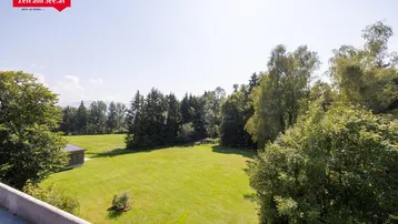 Weitläufige Grünfläche mit Bäumen und einem kleinen Gebäude im Hintergrund unter blauem Himmel.