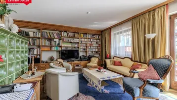 Gemütliches Wohnzimmer mit traditionellem Kachelofen, Bücherregal und klassischen Möbeln.