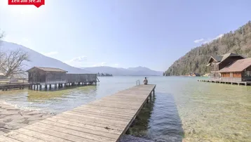 Langer Holzsteg führt ins klare Seewasser mit umliegenden Bergen und Bootshäusern.