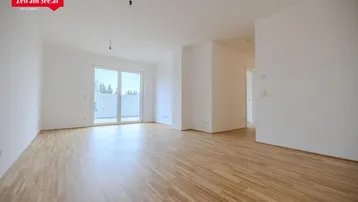 Heller, leerer Raum mit Parkettboden und Zugang zu einem Balkon oder einer Terrasse.