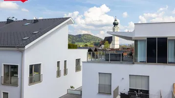 Dachterrasse mit Sitzgelegenheiten und Blick auf die umliegende Landschaft und Kirchturm.